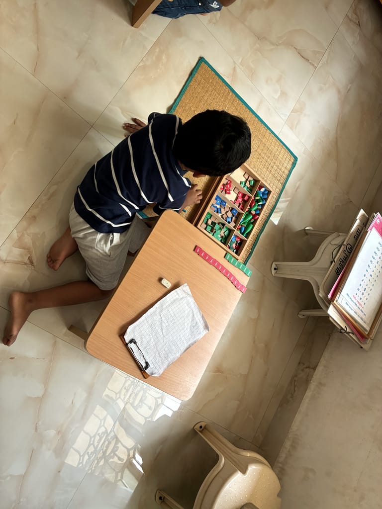 Seen from above, a child works with coloured bead bars at a small table.