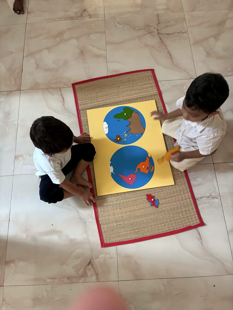 Two children explore colourful world map puzzles together on floor mats.