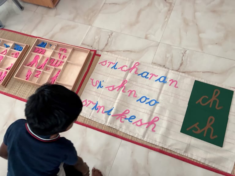 A child builds words with pink and blue movable letters on a floor mat.