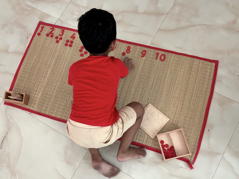 A child matches red counters to numerals from one to ten on a mat.